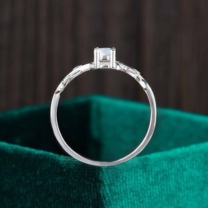 Op de afbeelding: Een zilveren ring met een enkele, heldere edelsteen gezet in een delicaat, bloemig ontwerp. De ring wordt getoond op een groene fluwelen achtergrond.