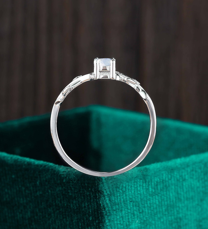 Op de afbeelding: Een zilveren ring met een enkele, heldere edelsteen gezet in een delicaat, bloemig ontwerp. De ring wordt getoond op een groene fluwelen achtergrond.