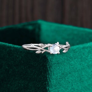Op de afbeelding: Een zilveren ring met een delicaat takontwerp en een ronde, heldere edelsteen. De ring ligt op een groene fluwelen achtergrond.