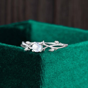 Op de afbeelding: Een zilveren ring met een heldere edelsteen gezet in een delicaat takontwerp. De ring ligt op een groene fluwelen achtergrond.