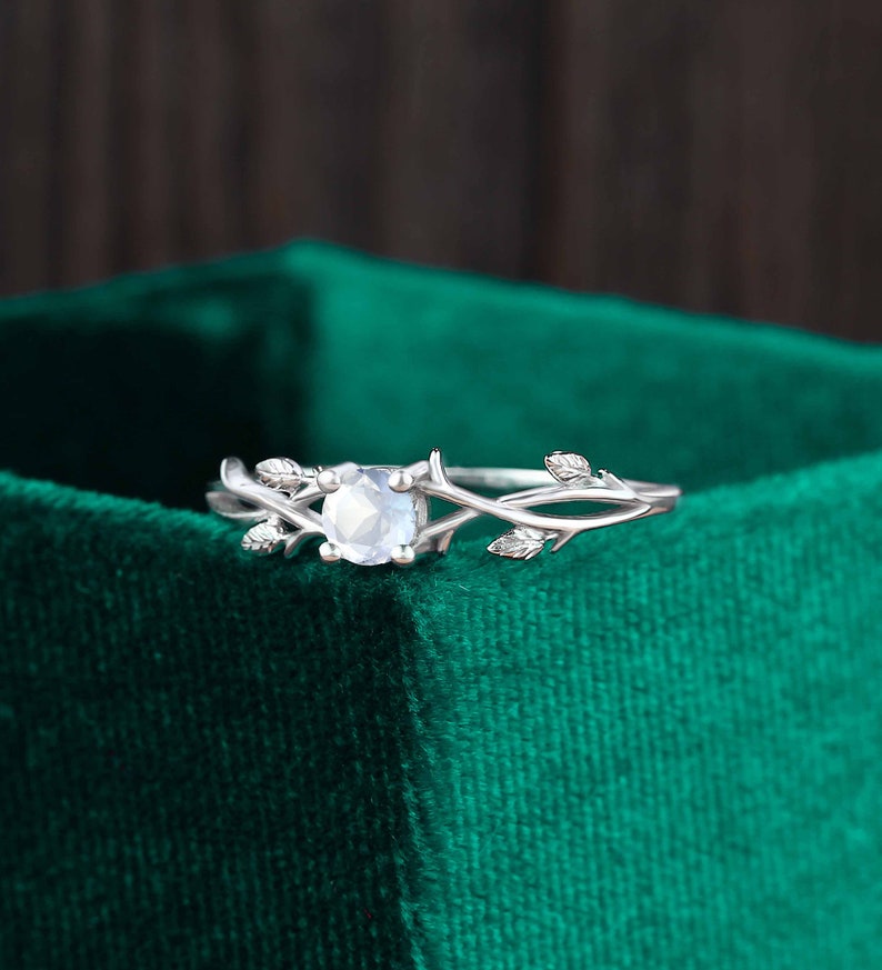 Op de afbeelding: Een zilveren ring met een heldere edelsteen gezet in een delicaat takontwerp. De ring ligt op een groene fluwelen achtergrond.