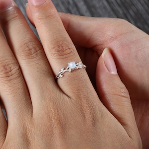 Op de afbeelding: Een zilveren ring met een delicaat rankontwerp en een ronde, heldere edelsteen in het midden.