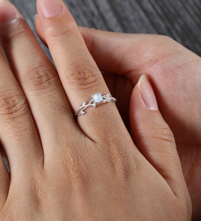 Op de afbeelding: Een zilveren ring met een delicaat rankontwerp en een ronde, heldere edelsteen in het midden.