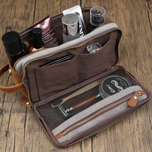 May include: Open brown leather toiletry bag with multiple compartments, zippers, and a handle. The bag is filled with various grooming products, including bottles, tubes, and a shaving kit. The bag is on a wooden surface.