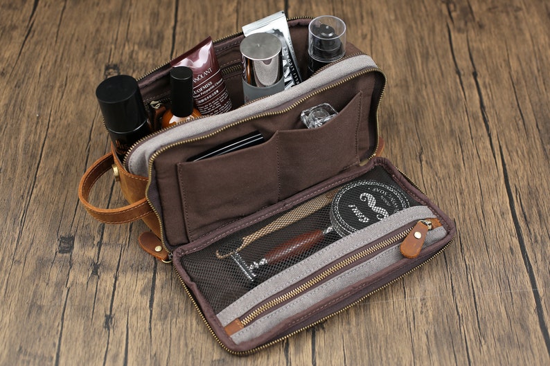 May include: Open brown leather toiletry bag with multiple compartments, zippers, and a handle. The bag is filled with various grooming products, including bottles, tubes, and a shaving kit. The bag is on a wooden surface.