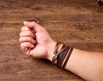 May include: A brown leather bracelet with a silver buckle. The bracelet is wrapped around a person's wrist.