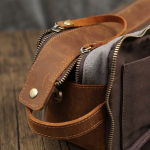 May include: A brown leather and canvas toiletry bag with a zipper closure and a handle. The bag has a brown leather exterior with a canvas interior and a brown zipper. The bag has a handle on the side.