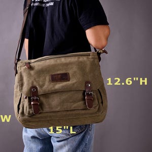 May include: An olive green canvas messenger bag with a brown leather flap closure, two front buckles, and a shoulder strap. The bag measures 15 inches long, 4.7 inches wide, and 12.6 inches high, featuring a rectangular shape and a dark leather patch.