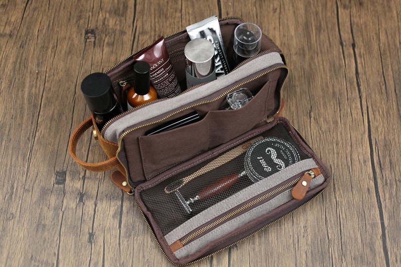 May include: Open brown toiletry bag with multiple compartments, filled with grooming products. The bag has a leather handle and a zippered closure. Inside are bottles, tubes, and a shaving kit.
