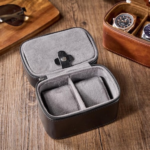 May include: A black leather watch box with two compartments lined with gray felt. The box is open and empty.