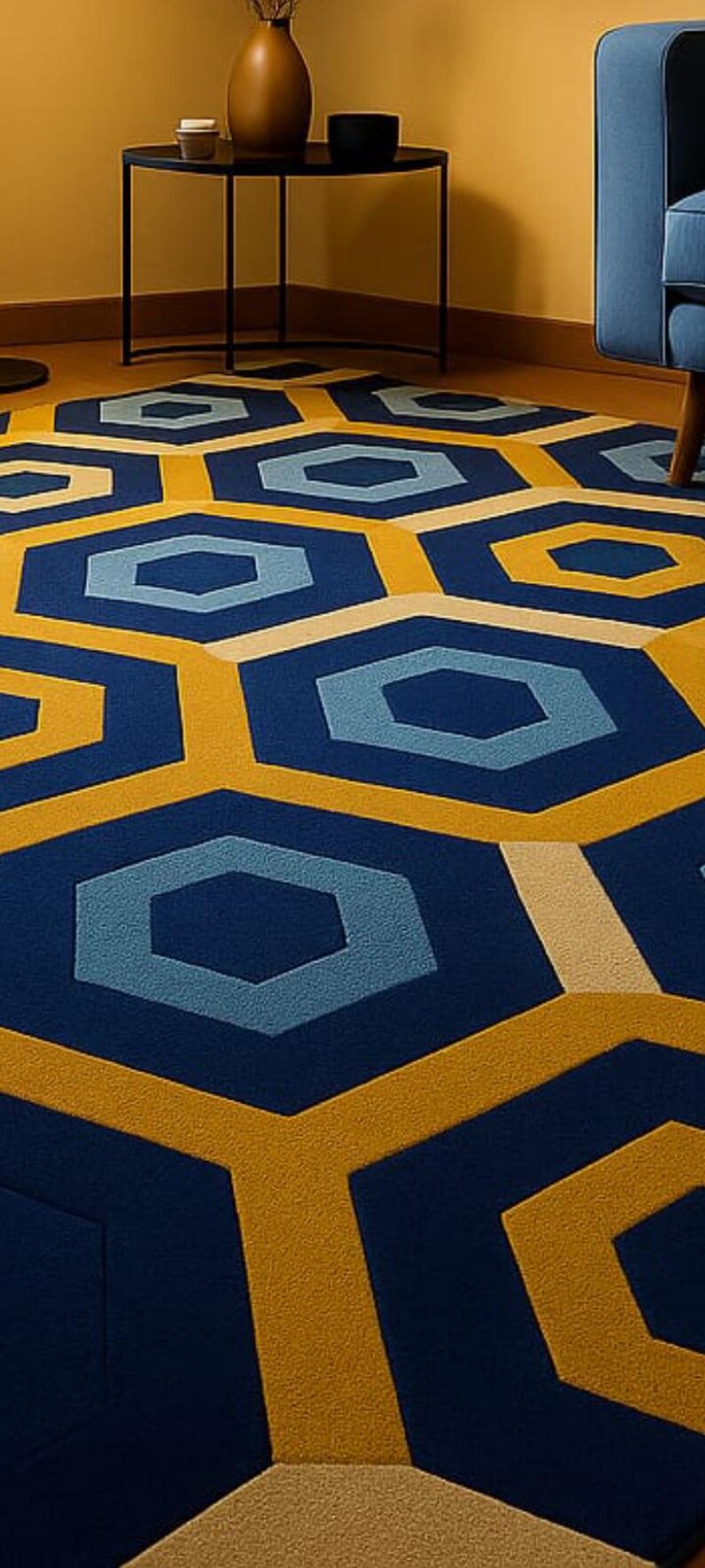 May include: A geometric patterned rug featuring a repeating hexagon design in navy blue, light blue, and gold. The rug is placed on a wooden floor, with a small black table and blue chair visible in the background.