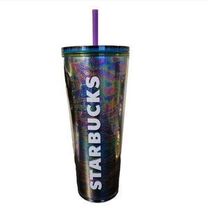 May include: A tall, iridescent Starbucks tumbler with a purple straw. The tumbler has a holographic finish with the Starbucks logo in white. The lid is dark blue. The tumbler is designed to hold cold beverages.