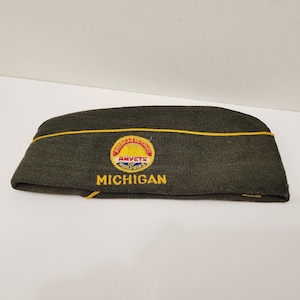 May include: A dark green military-style cap with a yellow trim and a circular patch. The patch reads "American Veterans of World War" and "Michigan" in yellow lettering. The cap is likely a vintage or collectible item.