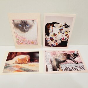 Op de afbeelding: Vier kunstprints met katten als thema. Eén print toont een Siamees met blauwe ogen en roze bloemen. Een andere toont een kat op een quilt. Een derde print toont een rustende kat. De laatste print toont een kat op een rieten stoel.