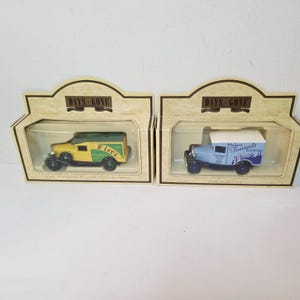 May include: Two die-cast model delivery trucks in display boxes. One is yellow and green with "Ivel" on the side. The other is light blue with "Madame Tussauds Exhibitions" on the side. Both are in boxes labeled "Days Gone".