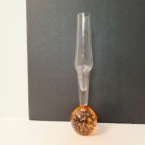 Op de afbeelding: Een hoge, heldere glazen vaas met een slanke, langwerpige hals die overgaat in een bolvormige voet. Het ronde onderste gedeelte is gemaakt van amberkleurig glas en is gevuld met talloze kleine, ingesloten luchtbelletjes.