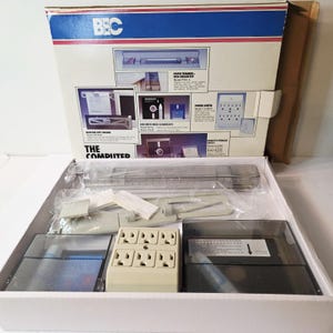 May include: An open box containing computer accessories, including a power strip, a paper trimmer, and disk drive head cleaner kits. The box is white with blue and red accents and the text "BEC" and "THE COMPUTER" printed on it.