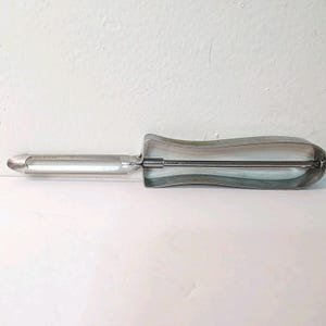 May include: A silver-toned potato peeler with a curved handle. The peeler has a blade on one end and a handle designed for a comfortable grip. The peeler is made of metal and is designed for kitchen use.