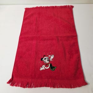 Puede incluir: Una toalla de mano roja con borde con flecos. Una imagen bordada de Mickey Mouse con un traje de Pap&aacute; Noel aparece en la toalla. La toalla est&aacute; hecha de un material suave y absorbente, ideal para el ba&ntilde;o o la cocina.