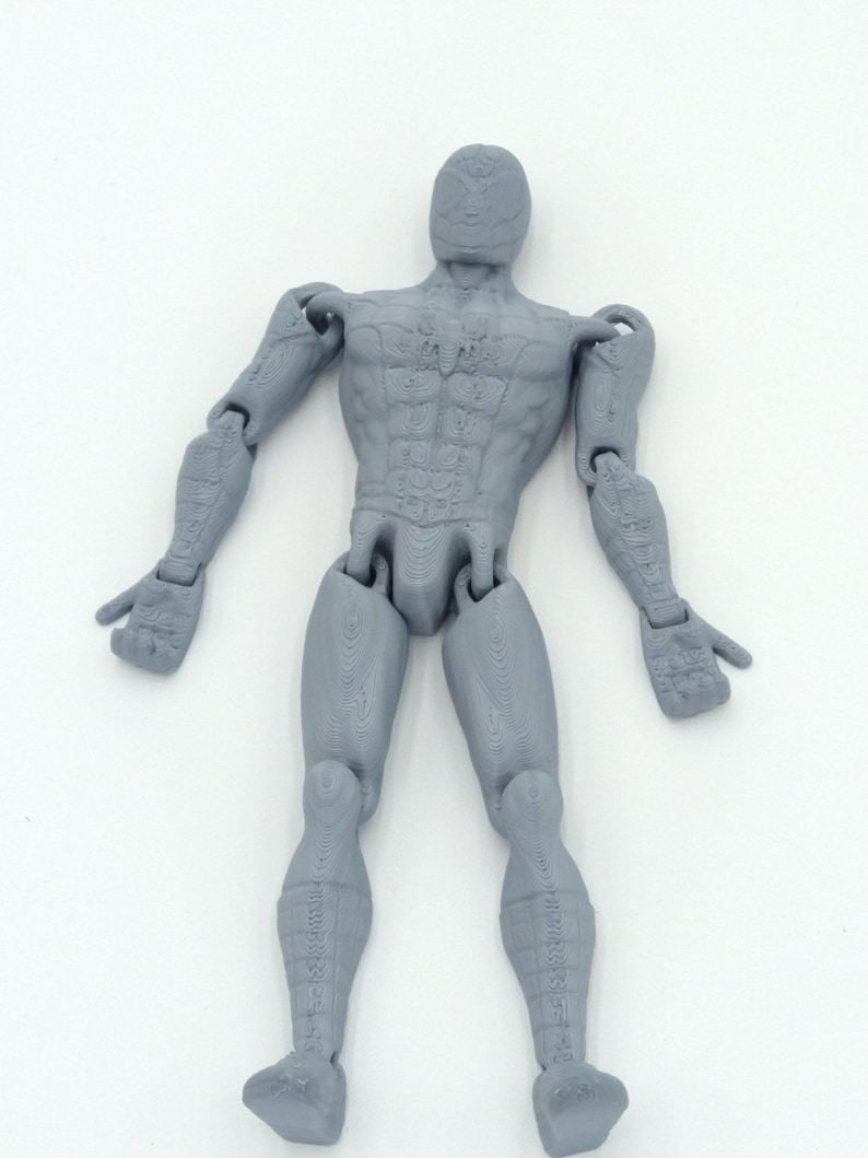 May include: A gray articulated action figure of a human form, with detailed musculature and jointed limbs. The figure is posed with arms outstretched and legs slightly apart, showcasing its range of motion. The figure is made of a solid gray material.