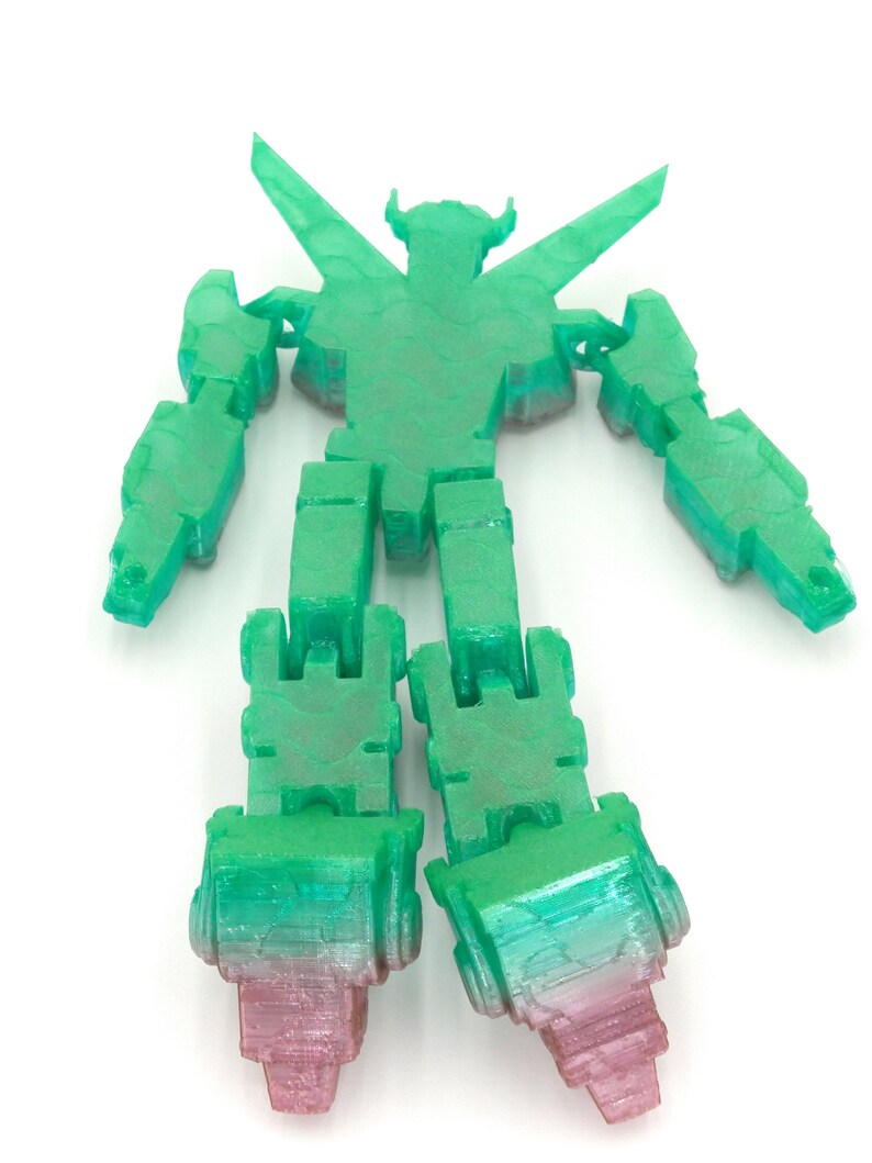 May include: A translucent green and pink robot toy with articulated limbs. The robot has a detailed, textured surface and a stylized design. The legs transition from green to pink. The robot is posed with arms and legs extended.