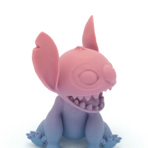 Puede incluir: Figura de dos tonos de un personaje alien&iacute;gena de dibujos animados. La cabeza y las orejas son rosas, mientras que el cuerpo y las extremidades hacen la transici&oacute;n de azul a morado. La figura tiene una boca muy abierta con dientes visibles y ojos grandes y expresivos.