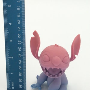 Puede incluir: Figura impresa en 3D de un personaje de dibujos animados, con cabeza y orejas rosas, cara y cuerpo morados, y manos y pies azules. La figura mide aproximadamente 7,6 cm de altura. El personaje tiene una amplia sonrisa dentada.