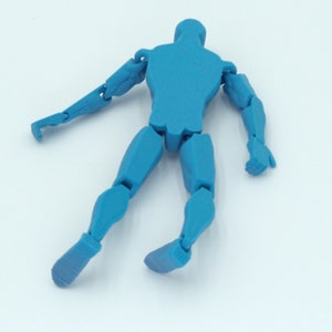 May include: A blue articulated figure with movable joints, posed in a dynamic stance. The figure is a solid, uniform color and appears to be made of plastic. The limbs are fully articulated, allowing for various poses. The figure is lying on a white surface.