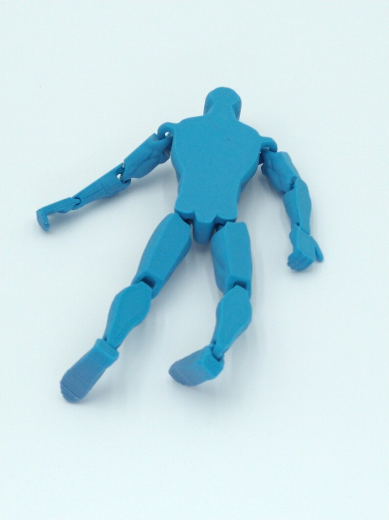 May include: A blue articulated figure with movable joints, posed in a dynamic stance. The figure is a solid, uniform color and appears to be made of plastic. The limbs are fully articulated, allowing for various poses. The figure is lying on a white surface.