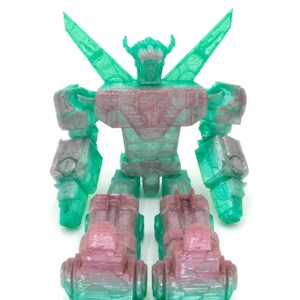 May include: A translucent, 3D-printed robot toy in shades of green and pink. The robot has a detailed design with articulated limbs, a head with horns, and large wing-like structures extending from its back. The toy is on a white background.