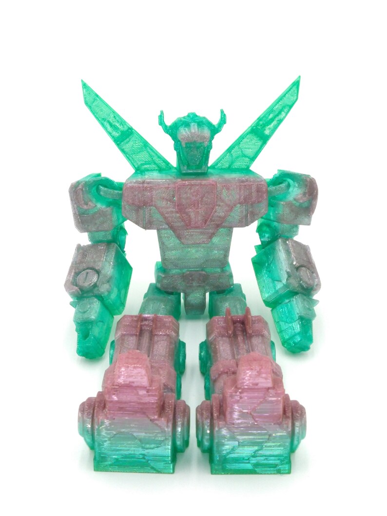 May include: A translucent, 3D-printed robot toy in shades of green and pink. The robot has a detailed design with articulated limbs, a head with horns, and large wing-like structures extending from its back. The toy is on a white background.