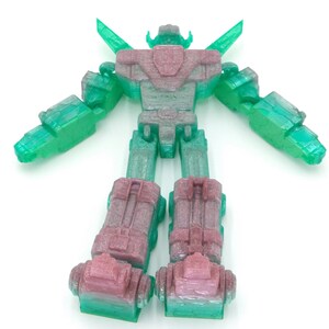 May include: A 3D-printed robot toy in shades of green and pink. The robot has a detailed design with articulated arms and legs, and a head with a distinctive shape. The toy is standing upright against a white background.