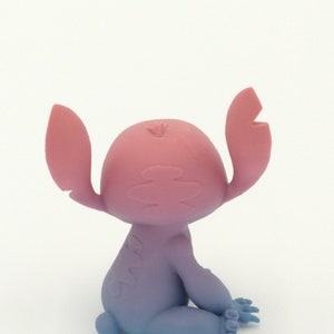 Puede incluir: Figura del personaje Stitch de la pel&iacute;cula animada Lilo & Stitch. La figura est&aacute; sentada con los brazos levantados. La cabeza y las orejas de la figura son rosas, con una transici&oacute;n a un cuerpo y piernas azules.