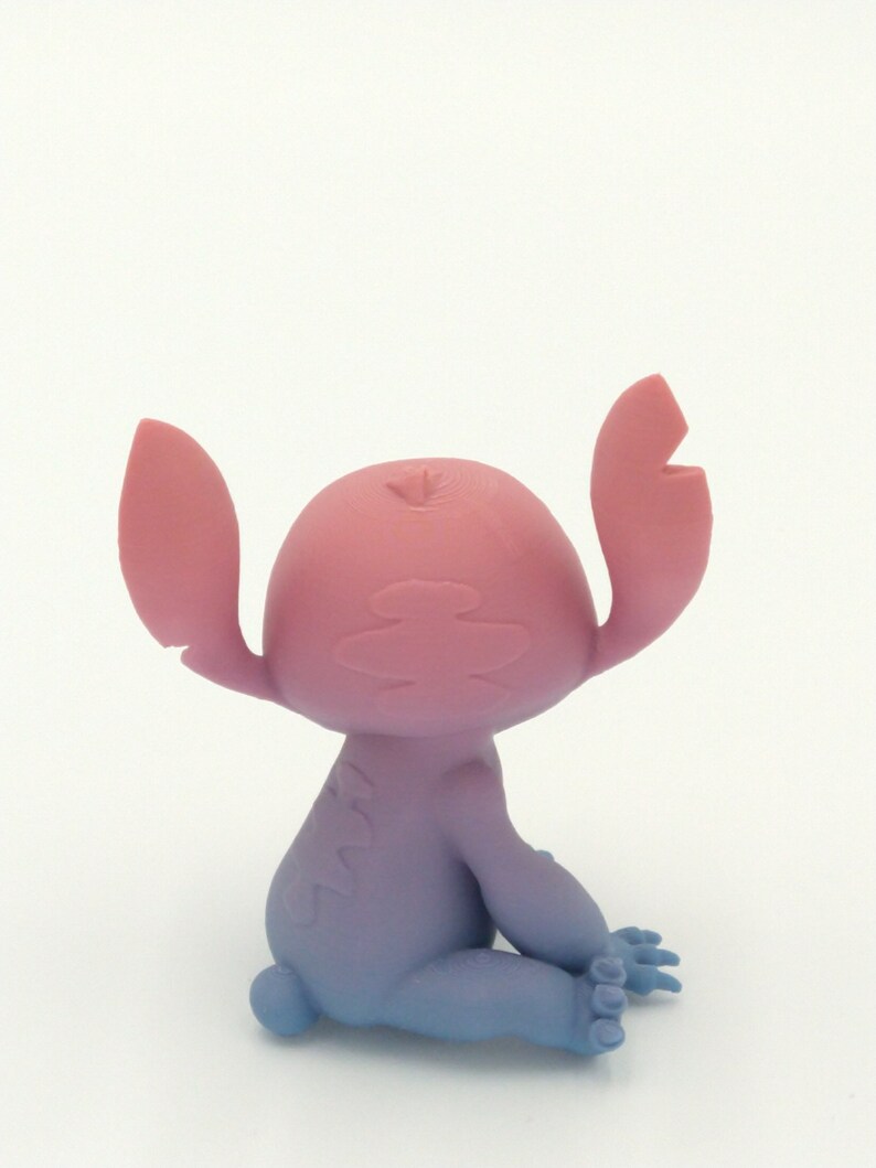 Puede incluir: Figura del personaje Stitch de la pel&iacute;cula animada Lilo & Stitch. La figura est&aacute; sentada con los brazos levantados. La cabeza y las orejas de la figura son rosas, con una transici&oacute;n a un cuerpo y piernas azules.