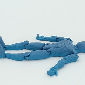 May include: A light blue articulated action figure of a humanoid character, lying on its back. The figure has detailed musculature and is made of plastic. The limbs are jointed for posing. The figure is on a white background.