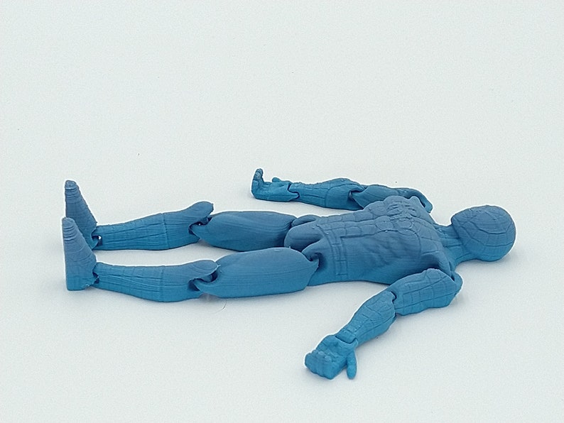 May include: A light blue articulated action figure of a humanoid character, lying on its back. The figure has detailed musculature and is made of plastic. The limbs are jointed for posing. The figure is on a white background.