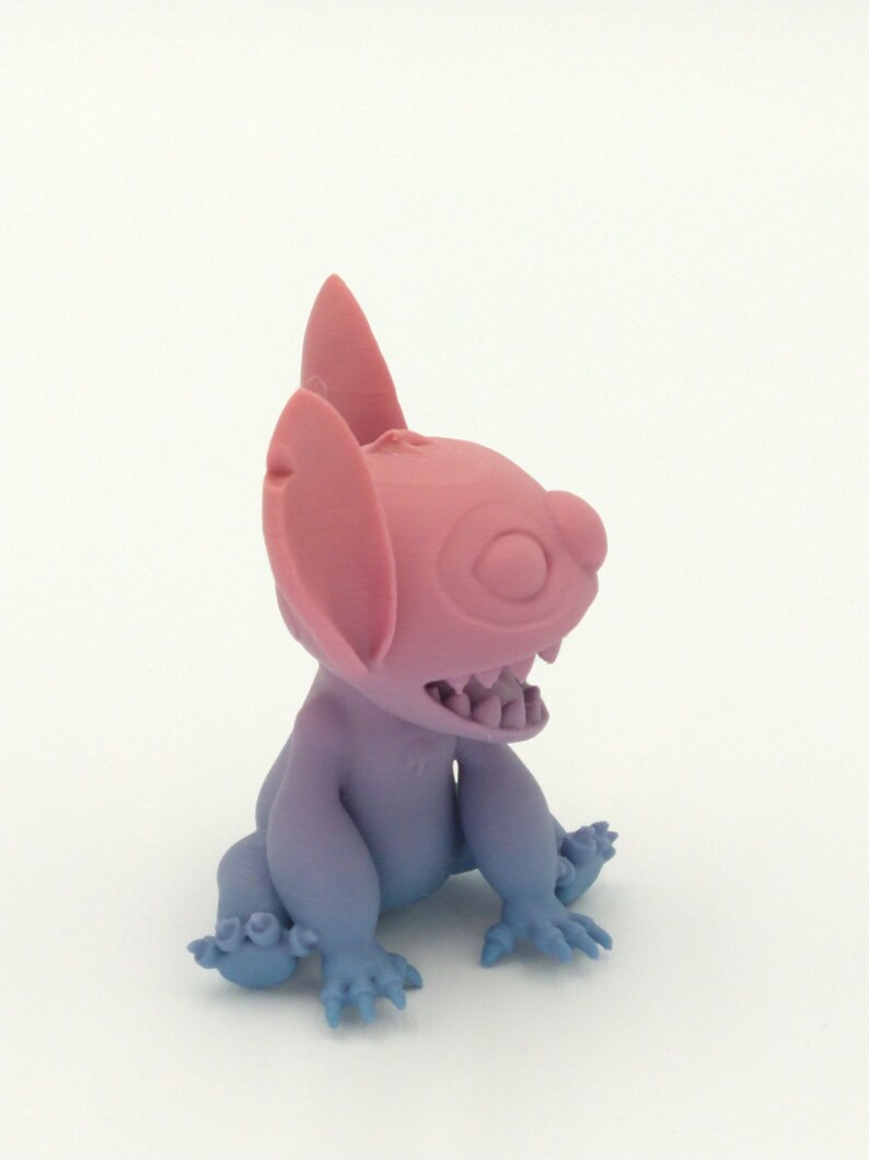 Puede incluir: Figura de un personaje de dibujos animados con grandes orejas y una sonrisa dentuda. La figura es un degradado de rosa y azul, con las orejas y la cabeza en rosa y el cuerpo y los pies en azul. Objeto de colecci&oacute;n.