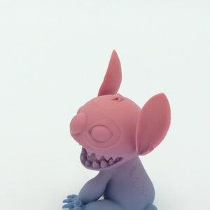 Puede incluir: Una figura rosa y azul de un personaje de dibujos animados con orejas grandes, una amplia sonrisa y cuatro dedos. La figura est&aacute; sentada con los brazos y las piernas doblados. Los colores hacen la transici&oacute;n de rosa a azul.