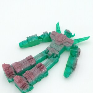 May include: A disassembled robot toy with a translucent green body and burgundy accents. The robot's limbs and torso are separated, showcasing its articulated design. The toy is set against a plain white background.