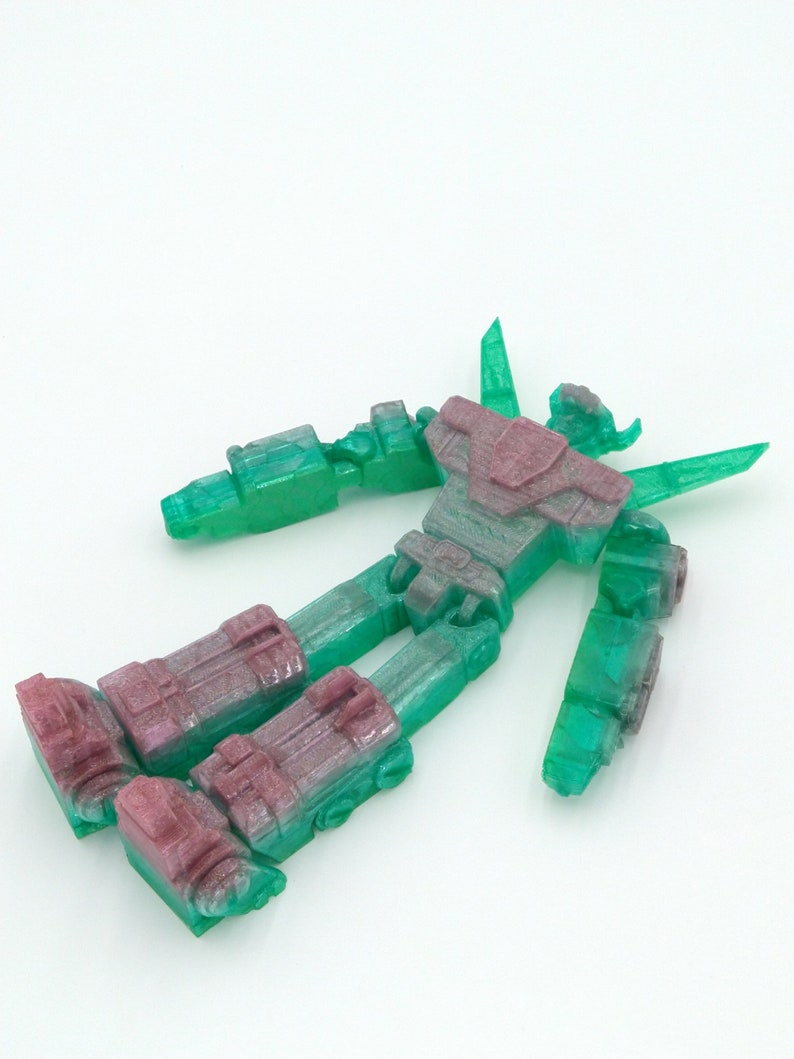 May include: A disassembled robot toy with a translucent green body and burgundy accents. The robot's limbs and torso are separated, showcasing its articulated design. The toy is set against a plain white background.