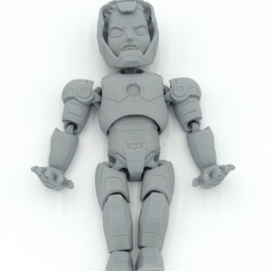 May include: A gray, articulated action figure of a superhero, featuring a helmeted head and detailed armor. The figure has movable arms, legs, and hands, and is posed against a white background. The figure is a collectible item.