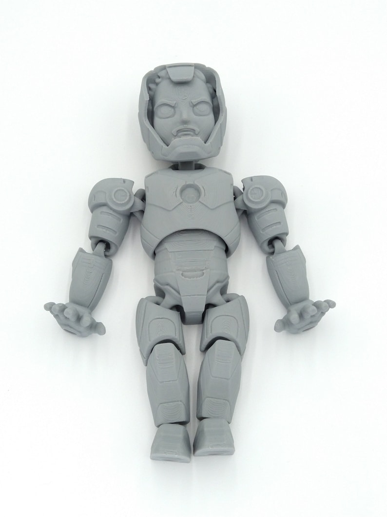 May include: A gray, articulated action figure of a superhero, featuring a helmeted head and detailed armor. The figure has movable arms, legs, and hands, and is posed against a white background. The figure is a collectible item.