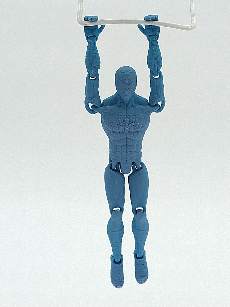 May include: A blue action figure of a superhero hanging from a white bar. The figure has a detailed design, with visible muscles and a spider emblem on the chest. The figure is suspended in mid-air against a white background.