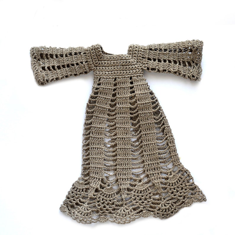 K&ouml;nnte beinhalten: Handgemachtes H&auml;kelkleid in neutralem Beige. Das Kleid hat lange &Auml;rmel und einen ausgestellten Rock mit einem detaillierten, strukturierten Muster. Das Kleidungsst&uuml;ck wird auf wei&szlig;em Hintergrund pr&auml;sentiert.
