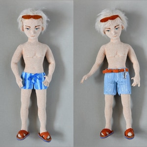 Può includere: Due bambole all'uncinetto con capelli bianchi, occhi azzurri e sandali marroni. Una bambola indossa pantaloncini da bagno a righe blu e bianche, l'altra indossa pantaloncini da bagno blu con una cintura marrone.