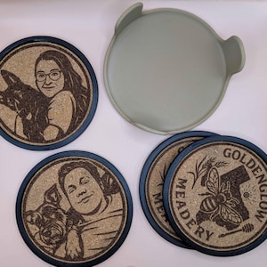 Puede incluir: Juego de posavasos redondos de corcho con bordes azul oscuro. Algunos posavasos presentan retratos grabados de personas con sus mascotas. Otros posavasos tienen el texto "GOLDENGLOW MEADERY" con una abeja y un mapa de California.