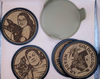 Può includere: Set di sottobicchieri rotondi in sughero con bordi blu scuro. Alcuni sottobicchieri presentano ritratti incisi di persone con i loro animali domestici. Altri sottobicchieri hanno il testo "GOLDENGLOW MEADERY" con un'ape e una mappa della California.
