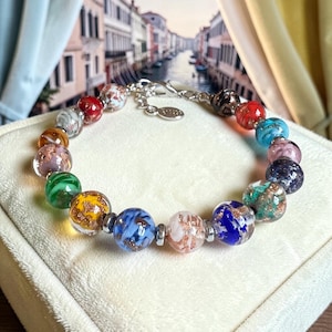 Op de afbeelding: Een veelkleurige kralenarmband met ronde glaskralen in tinten rood, blauw, groen, geel en roze, elk doordrenkt met metallic goudkleurige spikkels. De armband bevat kleine zilverkleurige metalen tussenstukjes en een zilverkleurige metalen sluiting.