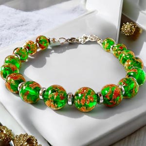 May include: A beaded bracelet featuring large, round, green glass beads with orange and gold flecks. The beads are strung on a silver-colored chain. A beautiful piece of jewelry.