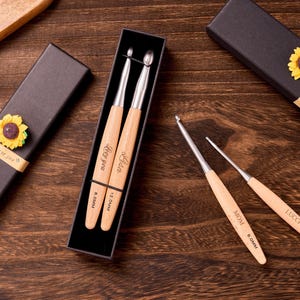 May include: A set of crochet hooks with wooden handles, some engraved with names and sizes. The hooks are in a black gift box with a sunflower accent. The wooden handles have the text "Love you", "Lisa", "MOM", and "Lucci".